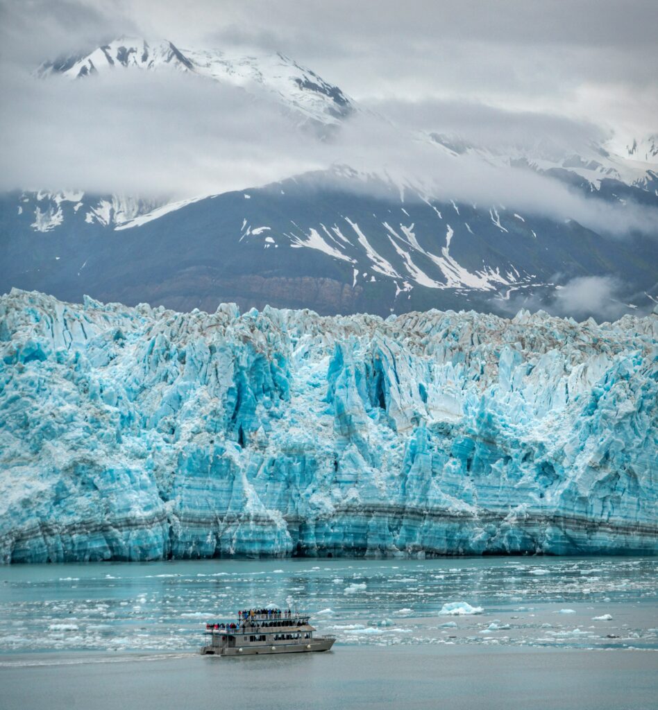 A little boat floats near the massive front of a glacier, demonstrating the size and grandeur of Alaska's frozen landscapes.